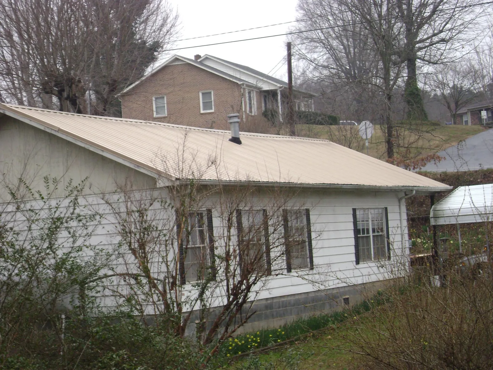 Tan metal roof on a white sided house set into a hillside — Commercial Roofing by Roofing Brothers in Marietta
